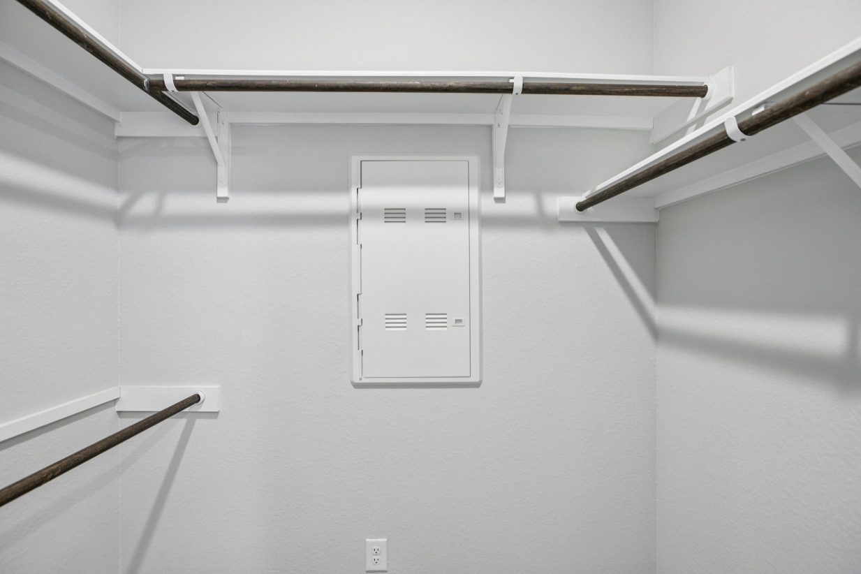 Image of the primary closet with light grey walls and wooden rods