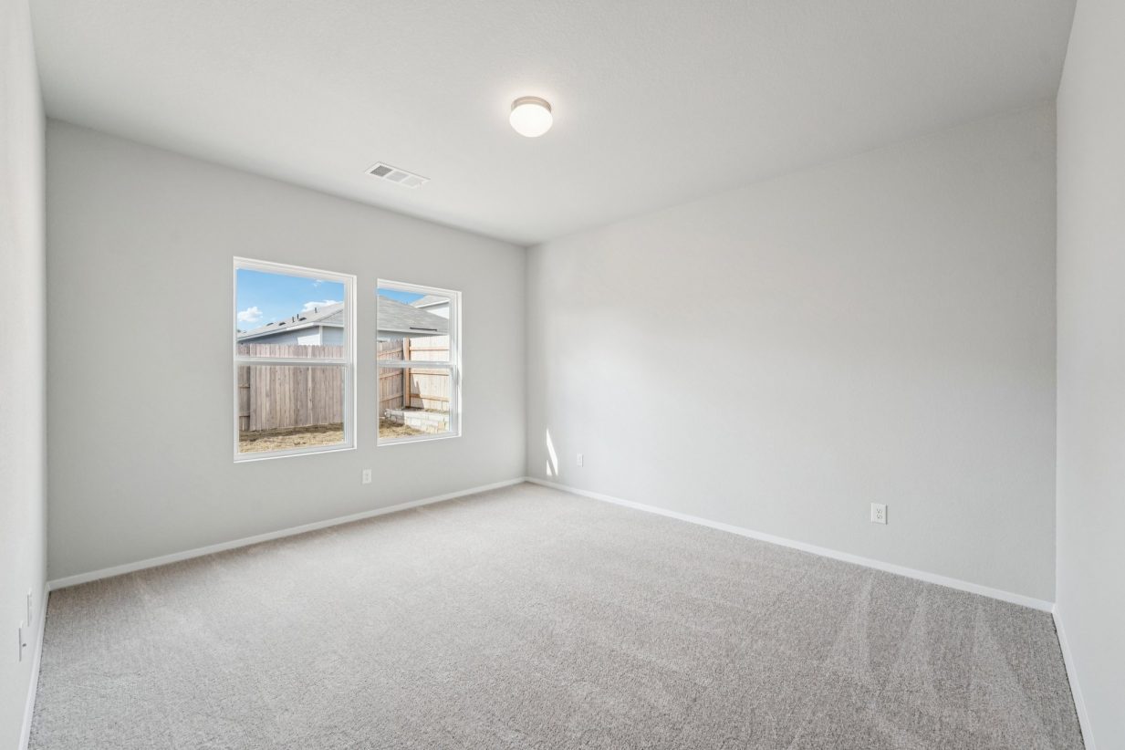 Image of a primary bedroom with light grey walls, tan carpeting, windows and white trim