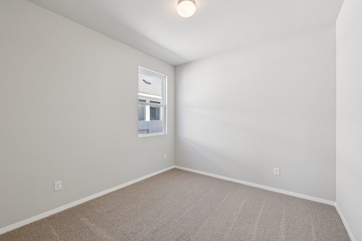 Image of a bedroom with light grey walls, tan carpeting and a window with white trim