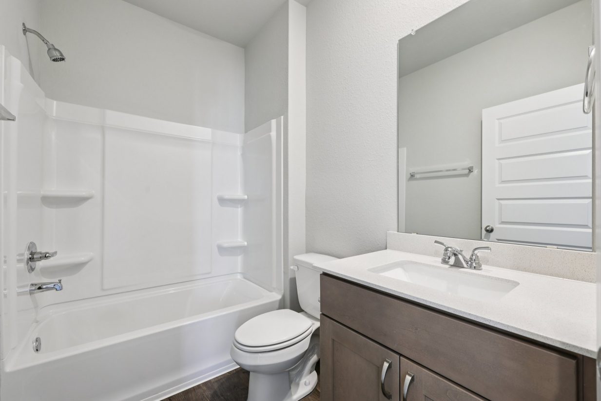 Image of a bathroom with brown cabinets, white countertops, a large mirror and a shower with a tub
