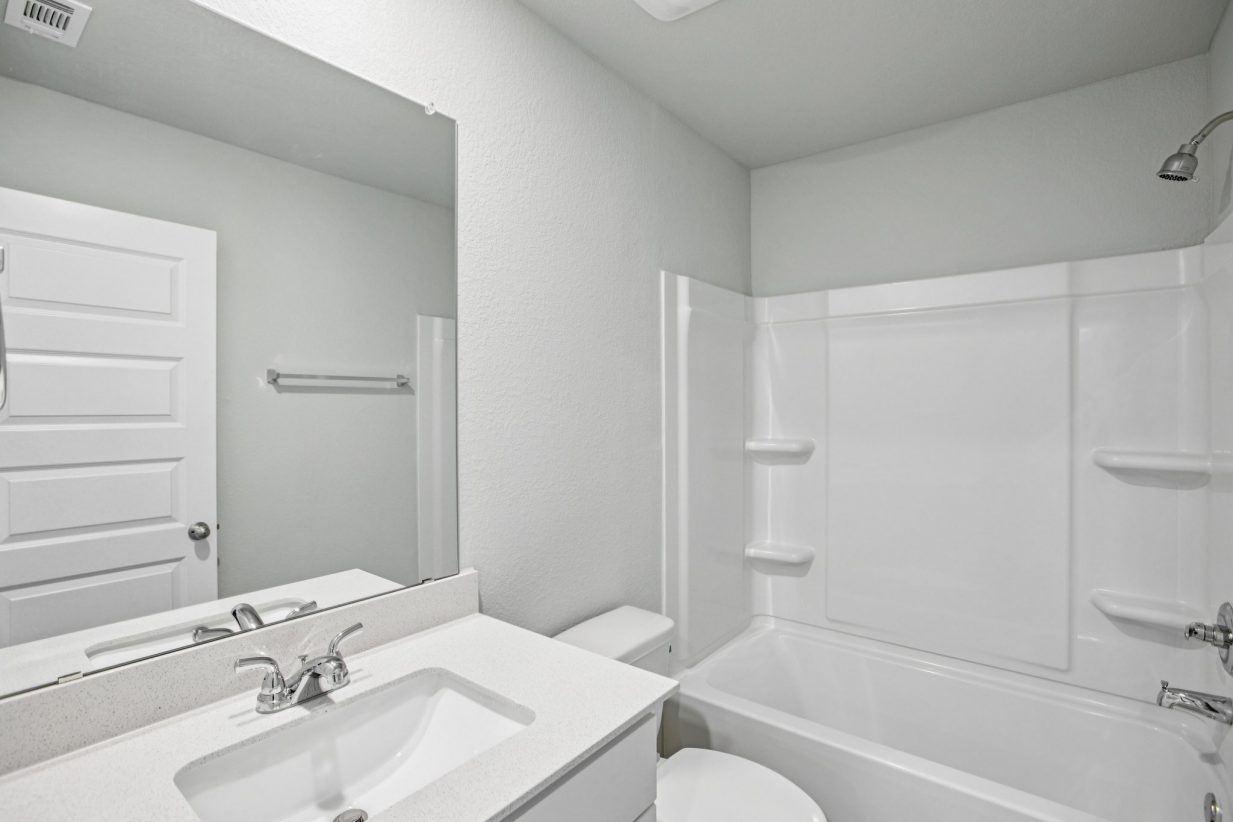 Image of a bathroom with light grey walls, a white vanity, a large mirror, and a white shower with a tub