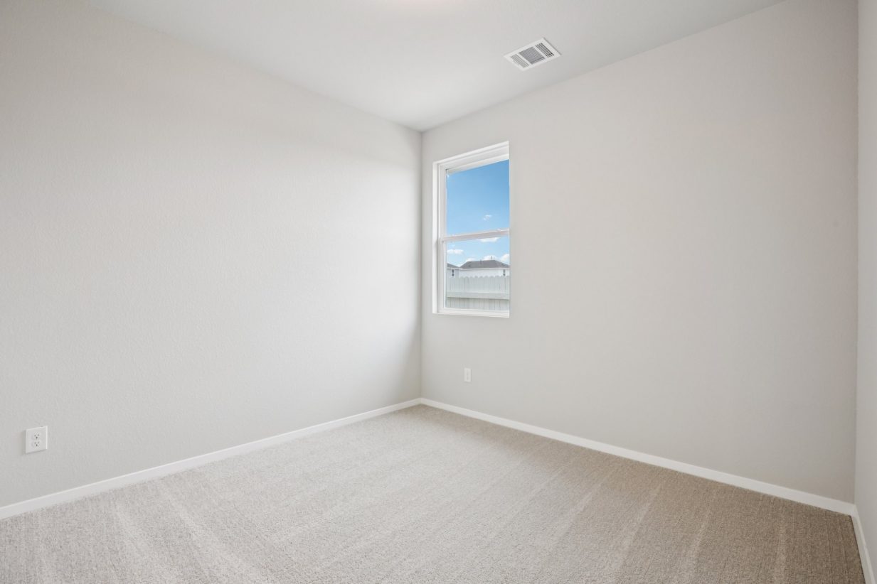 Image of a bedroom with light grey walls, tan carpeting, a window and white trim