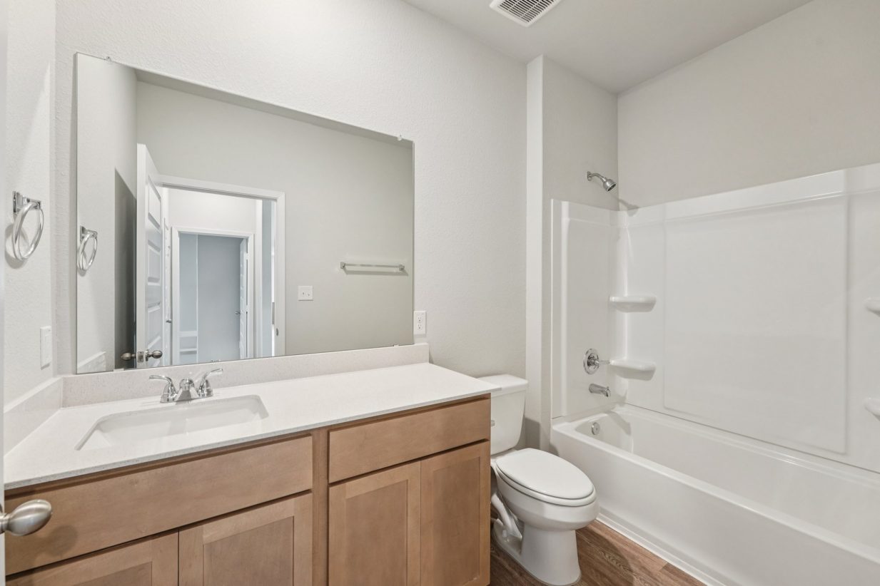 Image of a bathroom with a white vanity, brown cabinets, a large mirror and a shower and tub