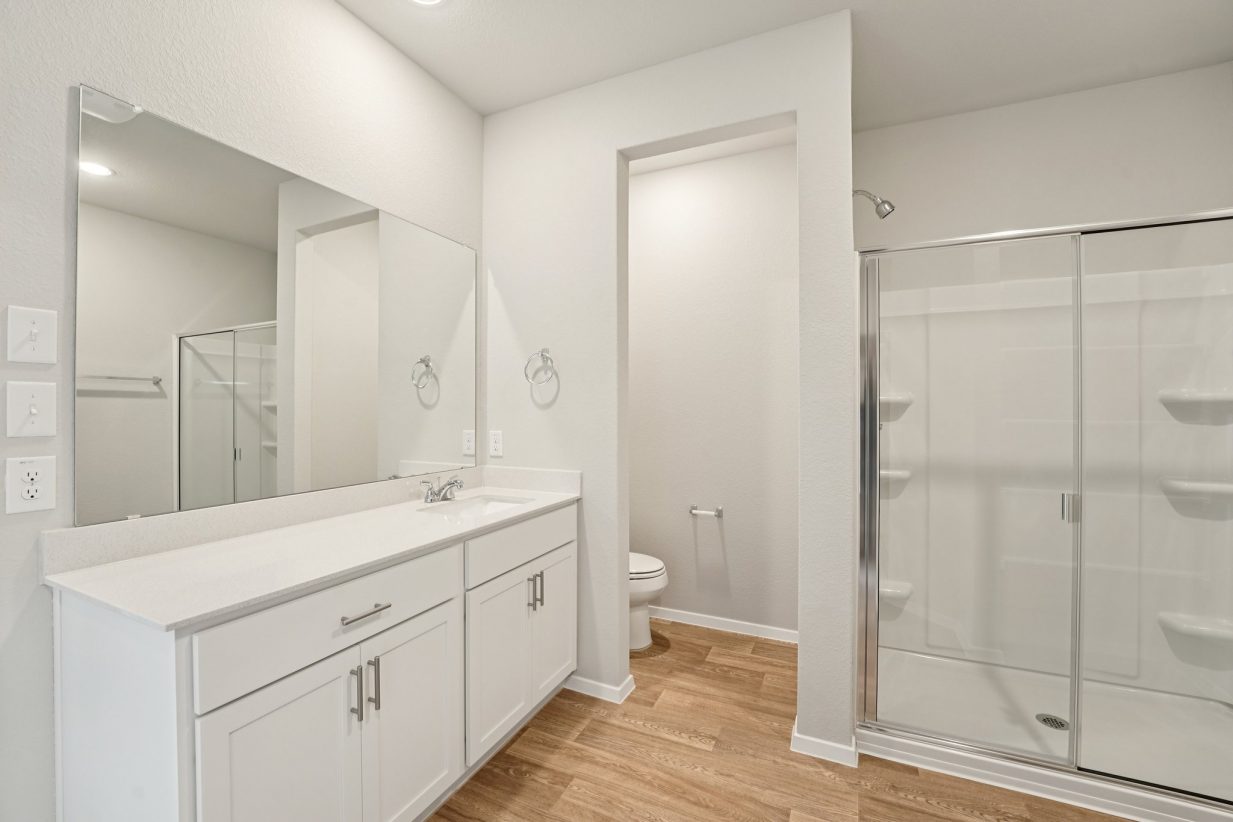 Image of a primary bedroom with a white dual vanity, white cabinets, a large mirror, and a standing shower and a semi-private water closet