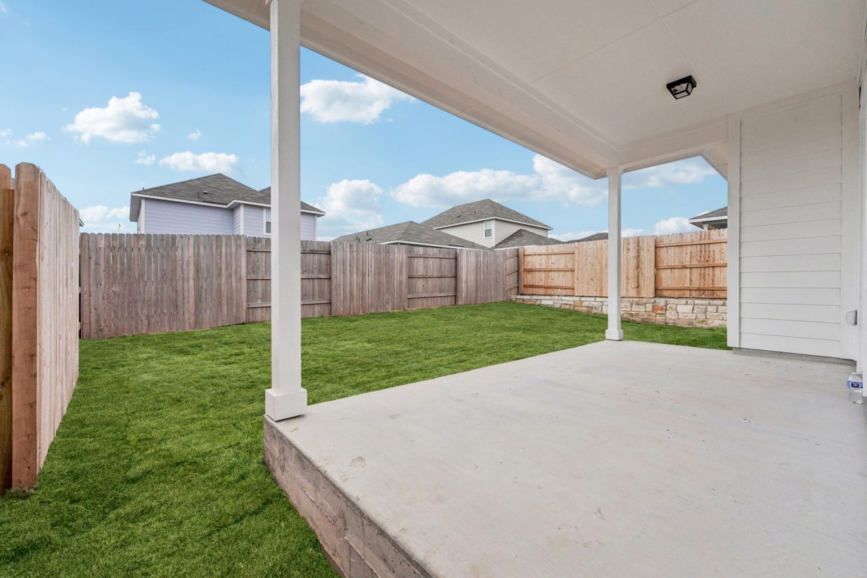 Image of the back exterior of a covered porch with a green grass back yard and a wooden fence
