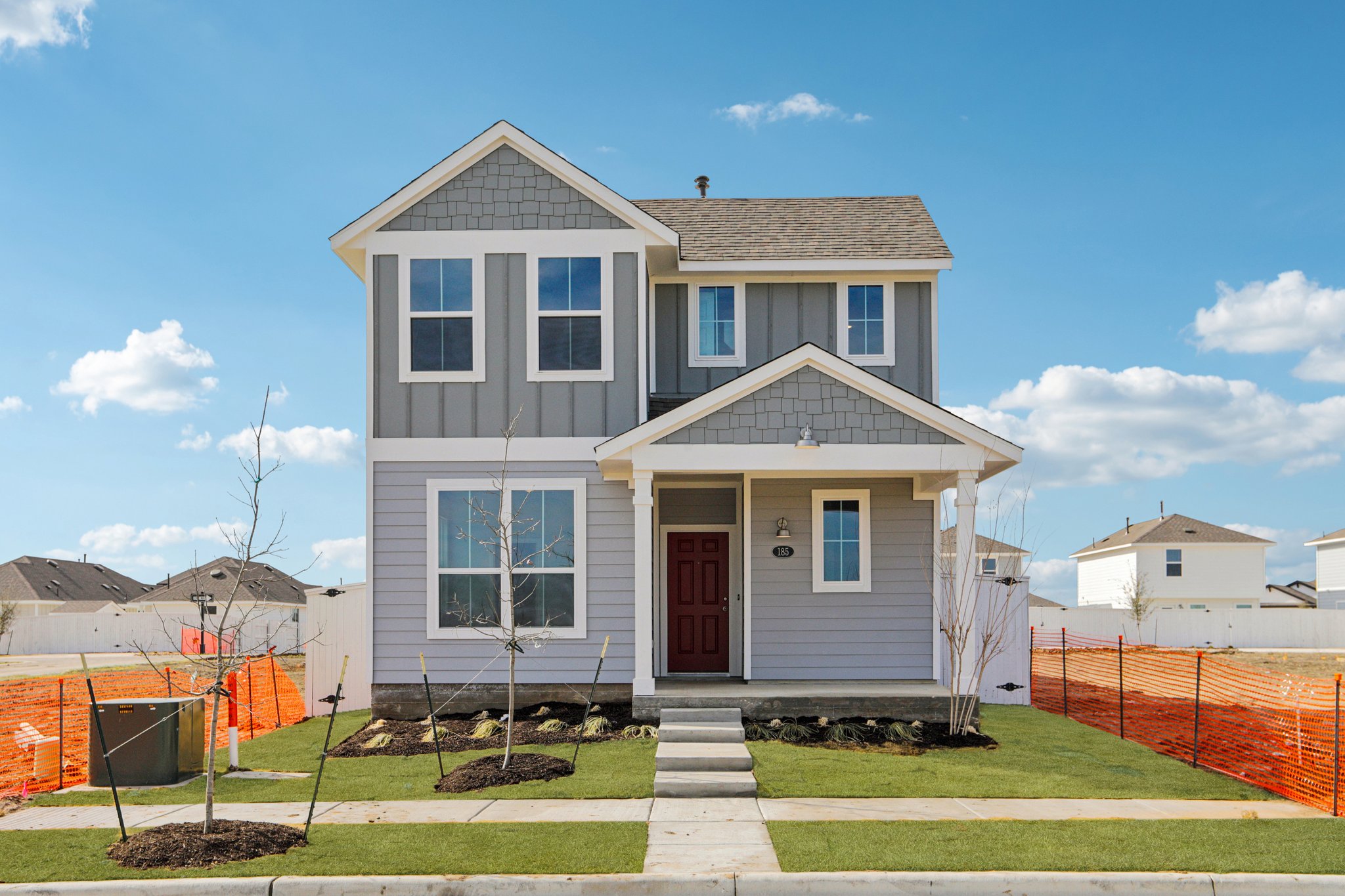 Image of the front exterior of a grey two story house with white trim, a red front door, a green grass front yard, and a blue sky in the background
