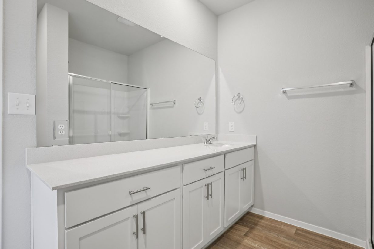Image of a primary bathroom with white cabinets, a dual white vanity, and a large mirror