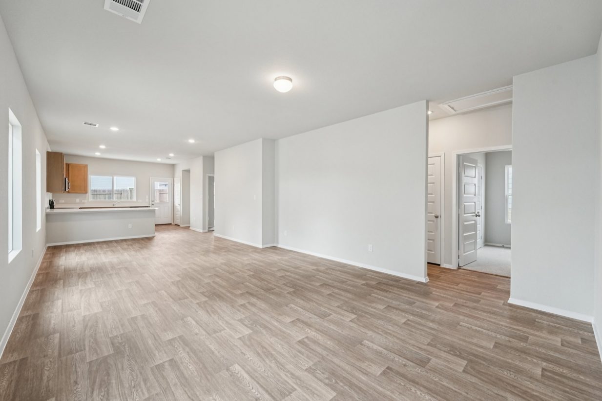 Image of a living room area with vinyl flooring, light grey walls, and a kitchen in the distance