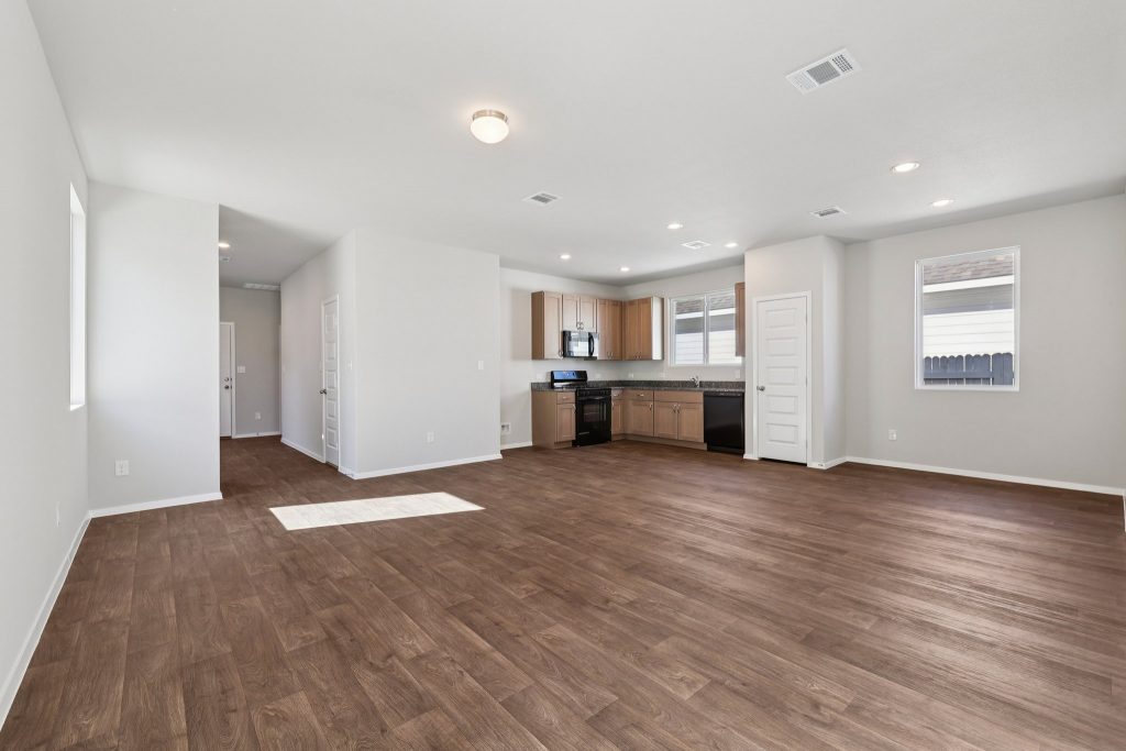 Image of a living room with grey walls, brown vinyl flooring and an L-shaped kitchen in the distance