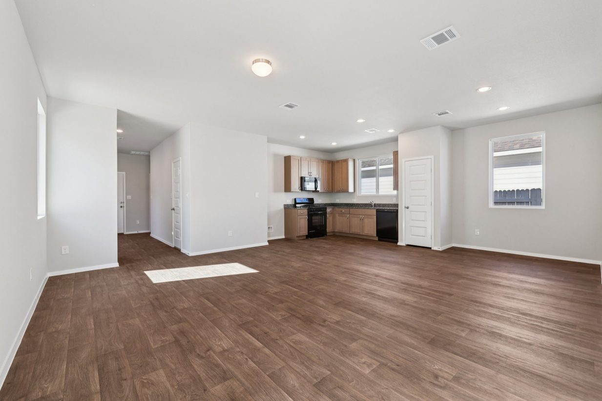 Image of a living room with grey walls, brown vinyl flooring and an L-shaped kitchen in the distance
