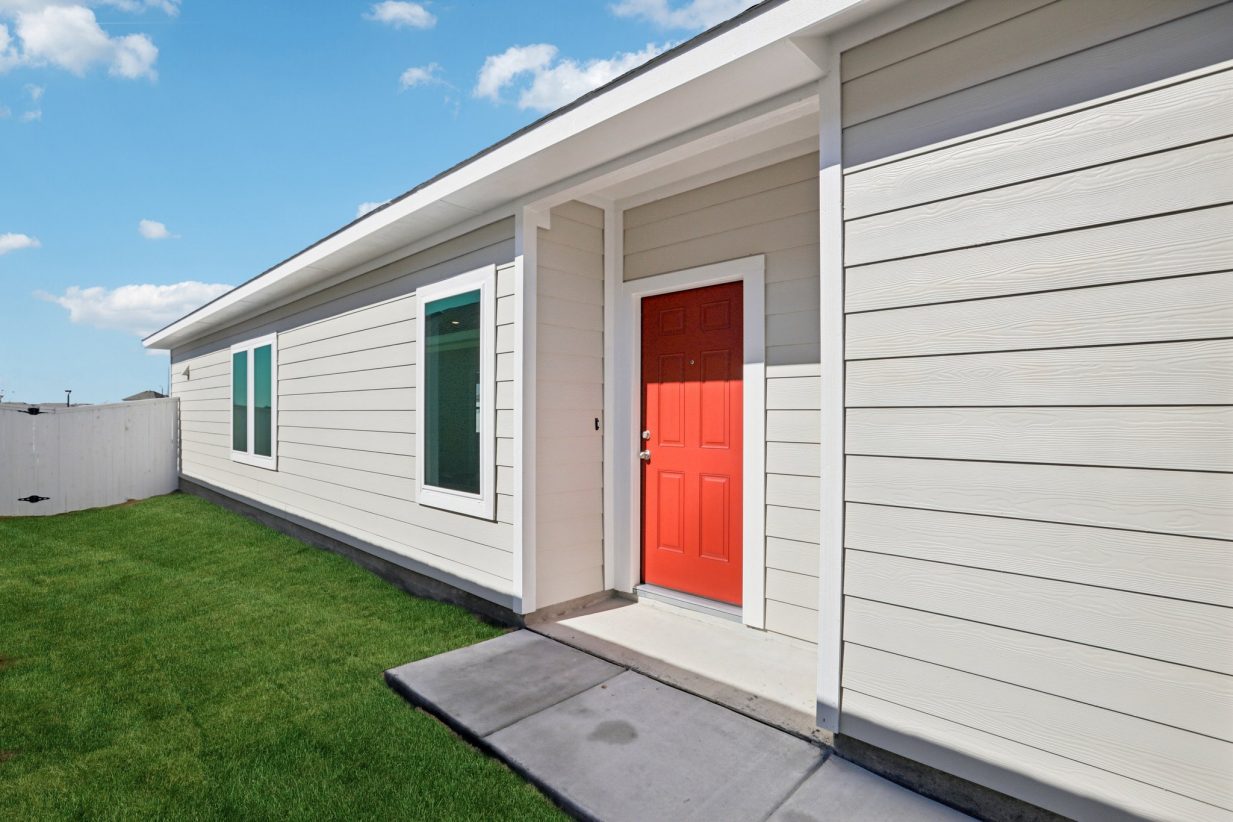 Image of a one story house red front door with a cement walk way and green grass