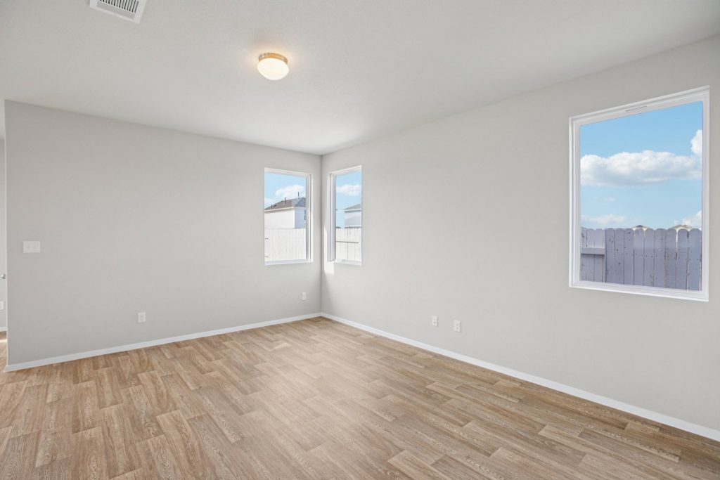 Image of a living room with light grey walls, light brown wood-look flooring, windows and white trim
