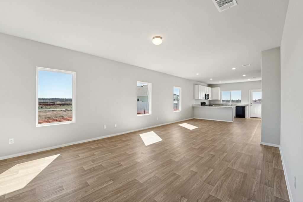 Image of a living room area with light grey walls, vinyl flooring, windows and white trim