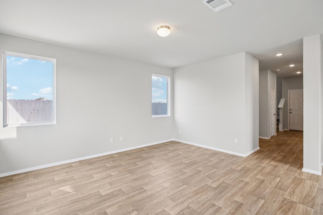 Image of a living room with light grey walls, light brown flooring, two windows, white trim