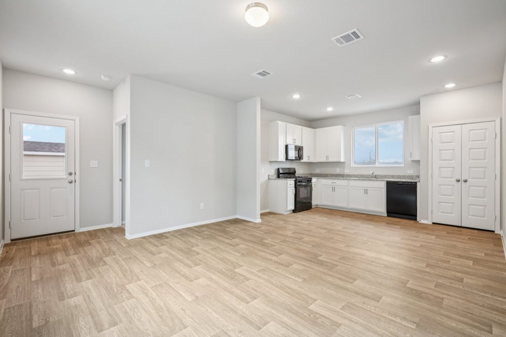 Image of a dining and living area with brown vinyl flooring, light grey walls, and an L-shaped kitchen