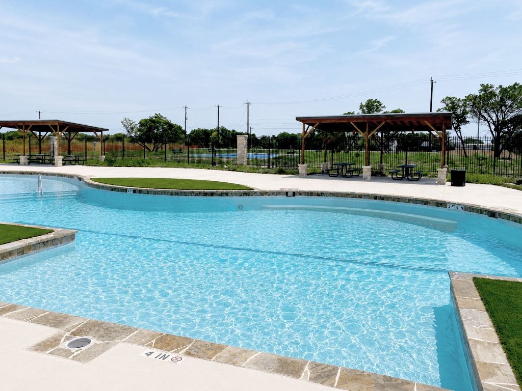 Photo of community pool with covered area behind and trees and grass