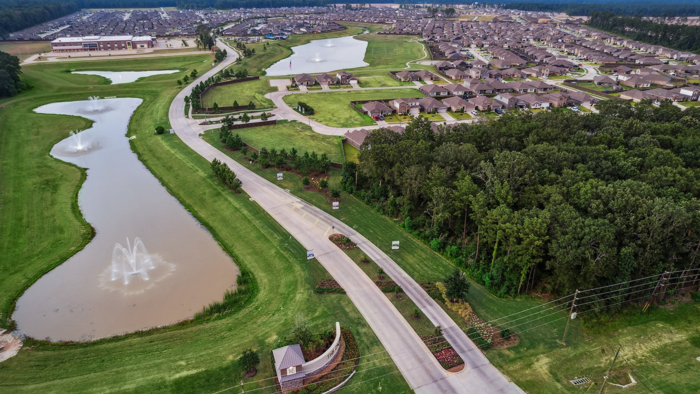Aerial image of a Brohn Homes Harrington Trails community showcasing a pond, green landscape, green trees, and homes with brown roofs.