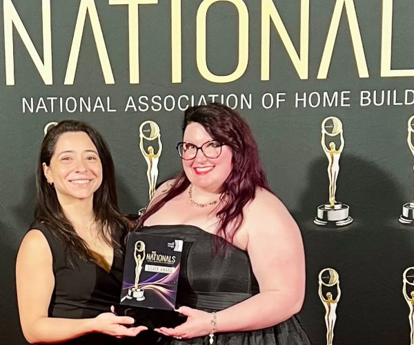 An image of two women. One with red hair and the other with brunette wearing black dresses in front of black backdrop with gold words "Nationals" and "National Association of Home Builders"