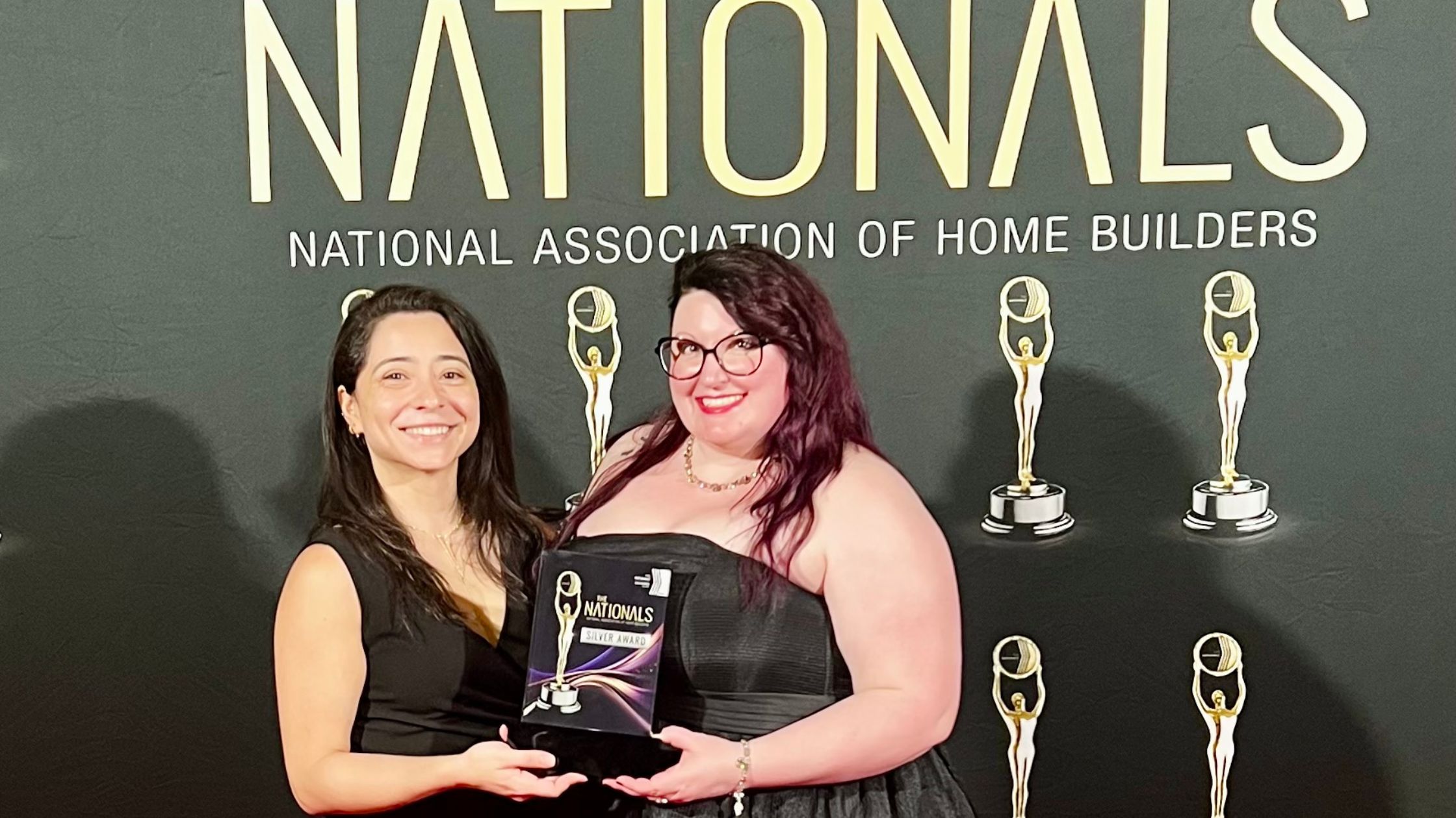 An image of two women. One with red hair and the other with brunette wearing black dresses in front of black backdrop with gold words "Nationals" and "National Association of Home Builders"