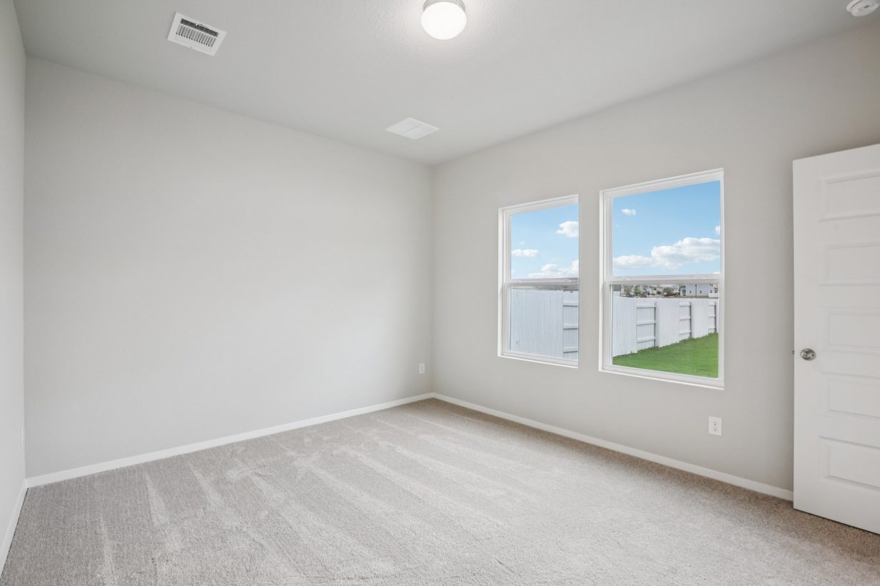 Image of a primary bedroom with light grey walls and tan carpeting