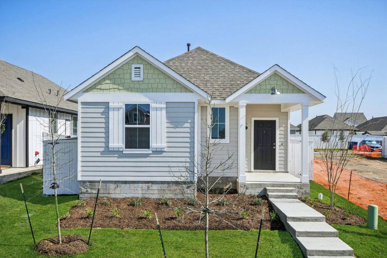 Image of a one story house with grey and green paint, a brown front foot and a cement pathway