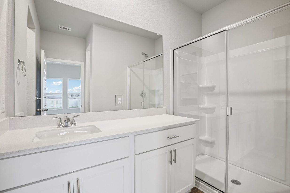 Image of a primary bedroom with a white double vanity, a large mirror and a standing shower