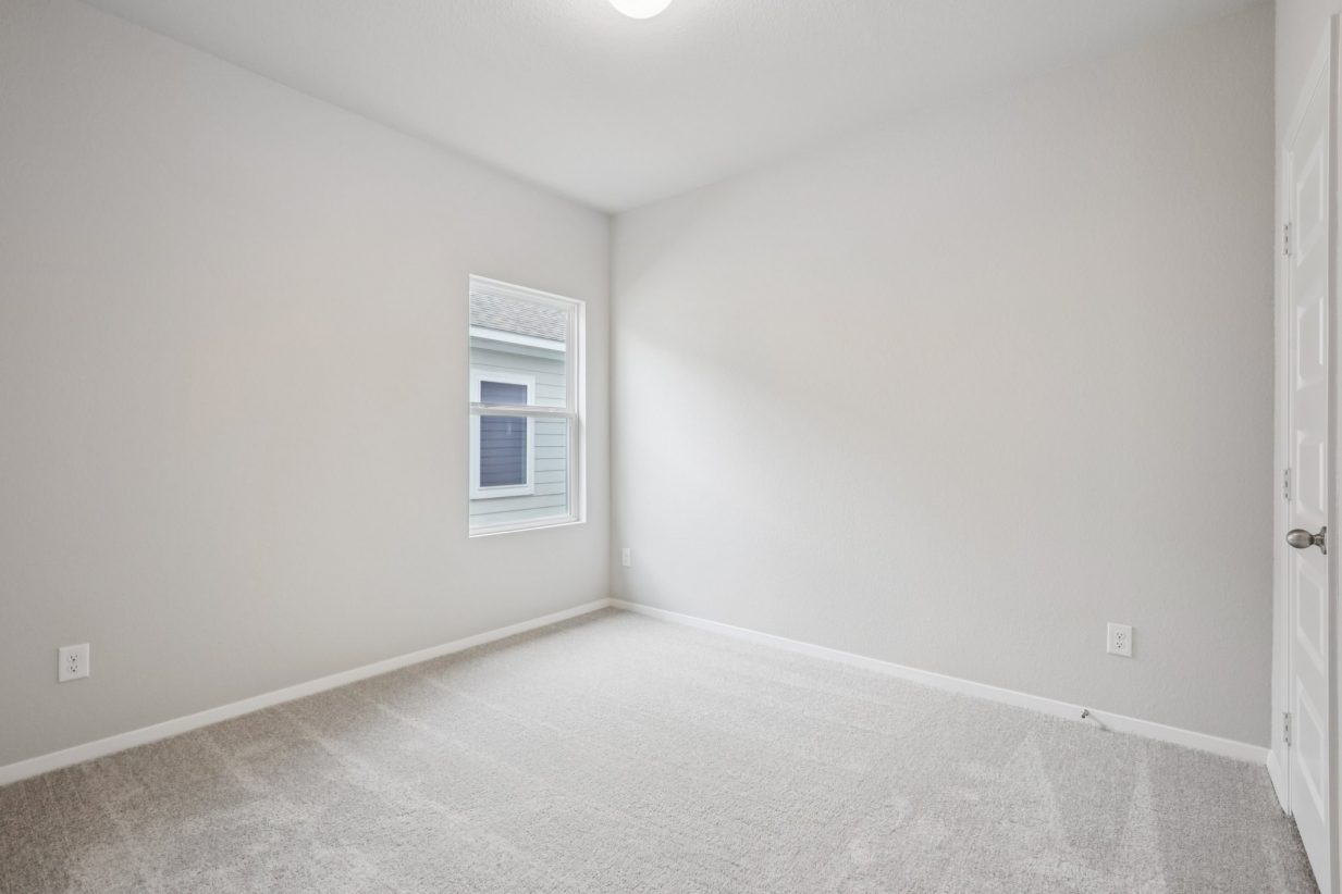 Image of a bedroom with light grey walls, tan carpeting and a window