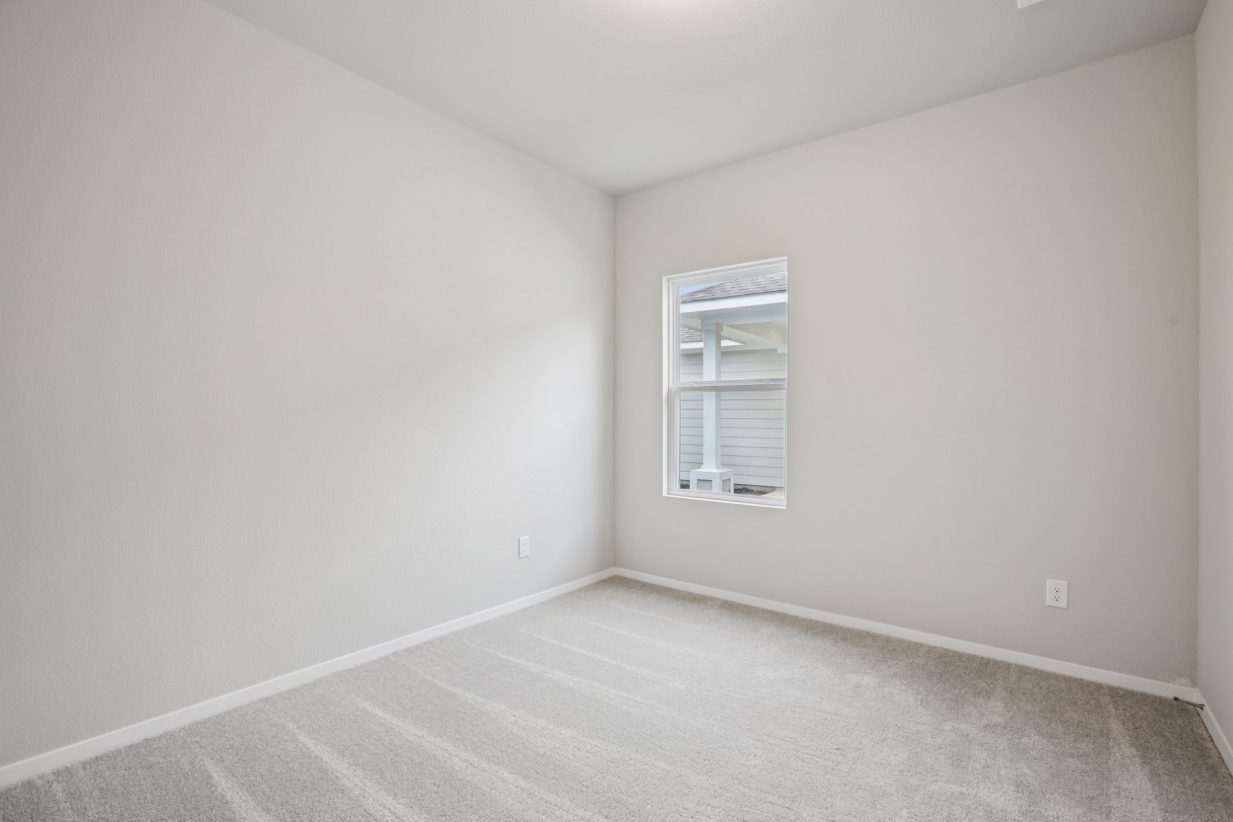 Image of a bedroom with light grey walls, tan carpeting and a window