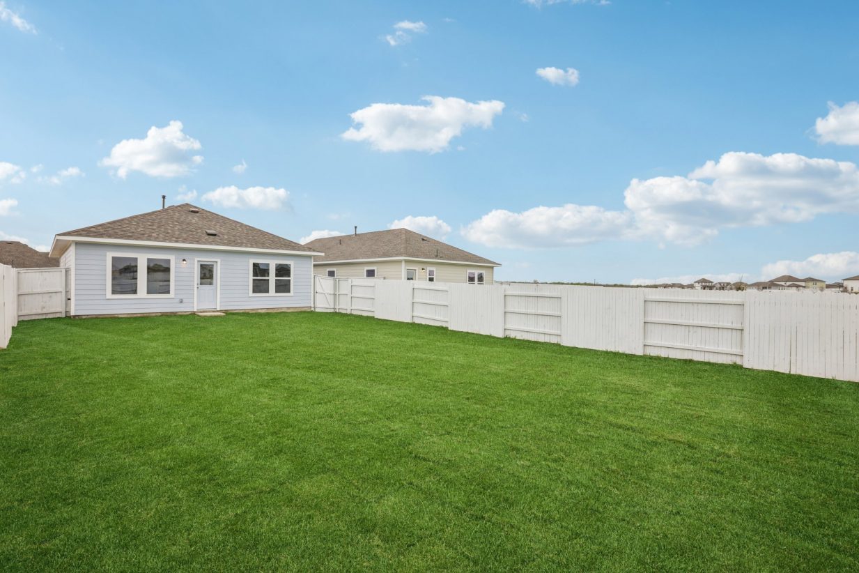 Image of a blue one story house back yard with a white fence