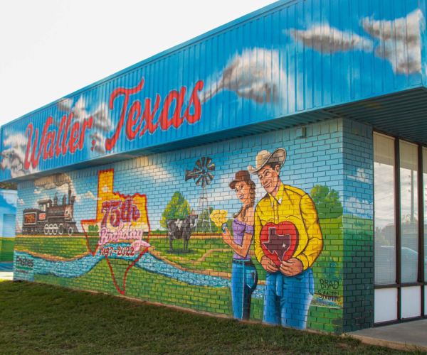 A vibrant and colorful mural with red words that say Waller, Texas, with a woman and man with greenery landscape, trees and a texas shape that says red in 75th.
