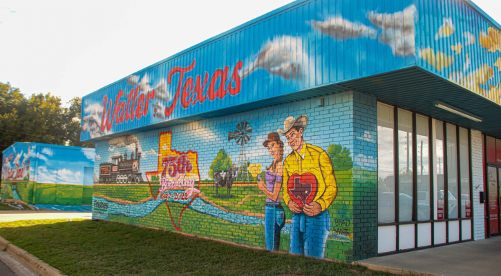 A vibrant and colorful mural with red words that say Waller, Texas, with a woman and man with greenery landscape, trees and a texas shape that says red in 75th.