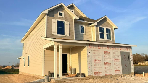An exterior of yellow two-story home underconstruction with windows and white framing and blue sky background.