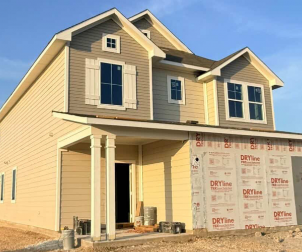 An exterior of yellow two-story home underconstruction with windows and white framing and blue sky background.