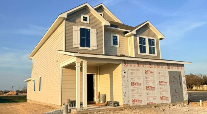 An exterior of yellow two-story home underconstruction with windows and white framing and blue sky background.