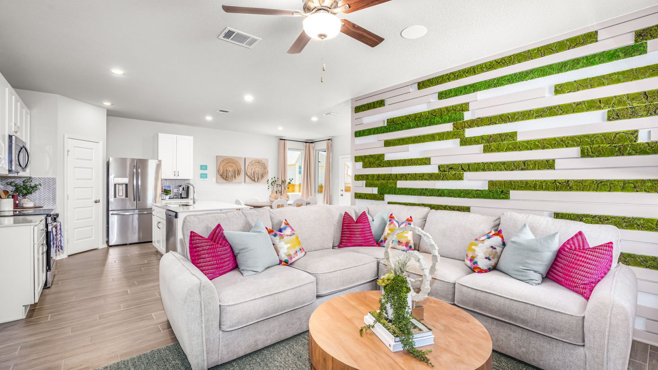 An image of living room with a white couch with bright pink pillows, tan coffee table, greenery, and a window with tan curtains.