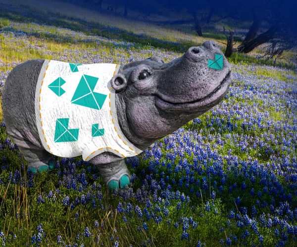 An image of gray hippo statue with a teal Brohn heart on its nose and a white t-shirt covered in teal hearts. The hippo is surrounded by a green landscape with blue bonnets.