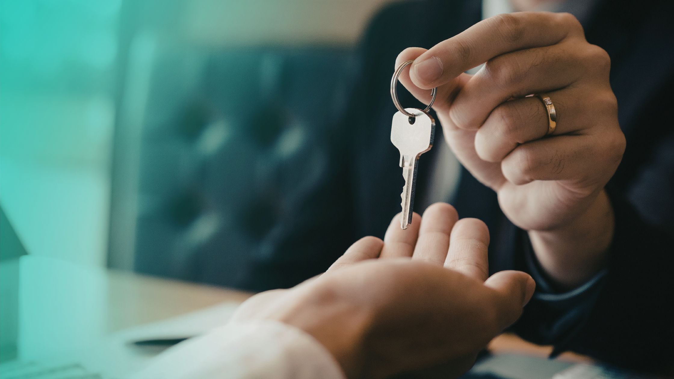 A closeup image of a hand with a wedding ring handing a key over to another person's hand.