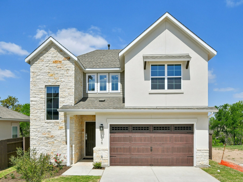 Exterior image of two-story with tan brick exterior, windows, brown garage door, with a concrete driveway and green landscape with a blue sky with clouds in the background.