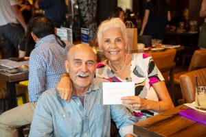 Image of a sitting couple smiling with a woman holding an envelope labeled "TopAgent Winner"
