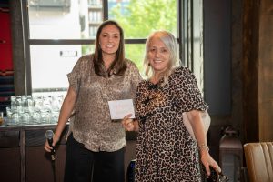 Image of two women standing and smiling, one woman is holding an envelope marked "TopAgent Winner"