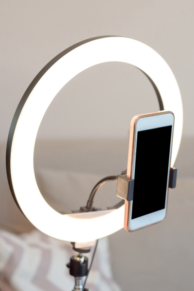 A close-up of ring light with a rose gold iPhone with a background of tan couch and tan and white chevron pillow.