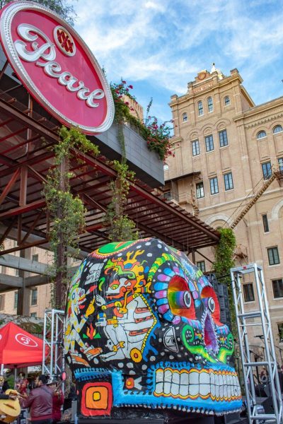 Image of Dias De Los Muertos celebration at the Historic Pearl featuring a colorful and artistic large skull with a pink and white circle sign with cursive white text that says "Pearl".
