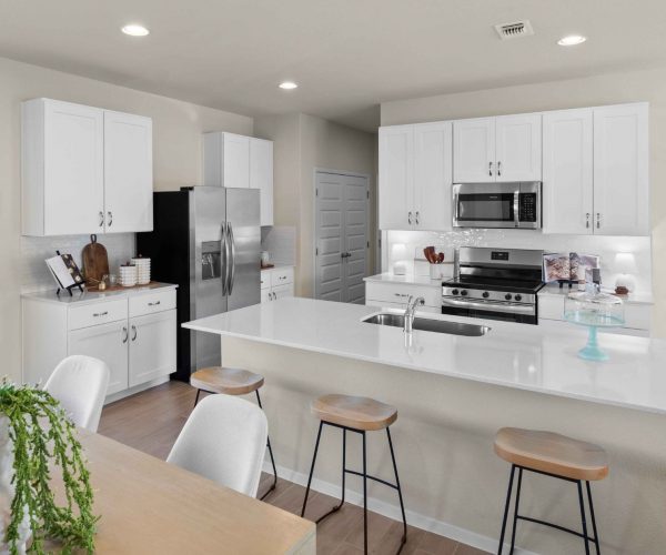 An interior image of a tan dining table view of the kitchen with vinyl flooring, white cabinets and countertop.