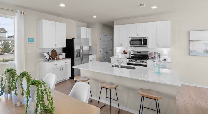 An interior image of a tan dining table view of the kitchen with vinyl flooring, white cabinets and countertop.