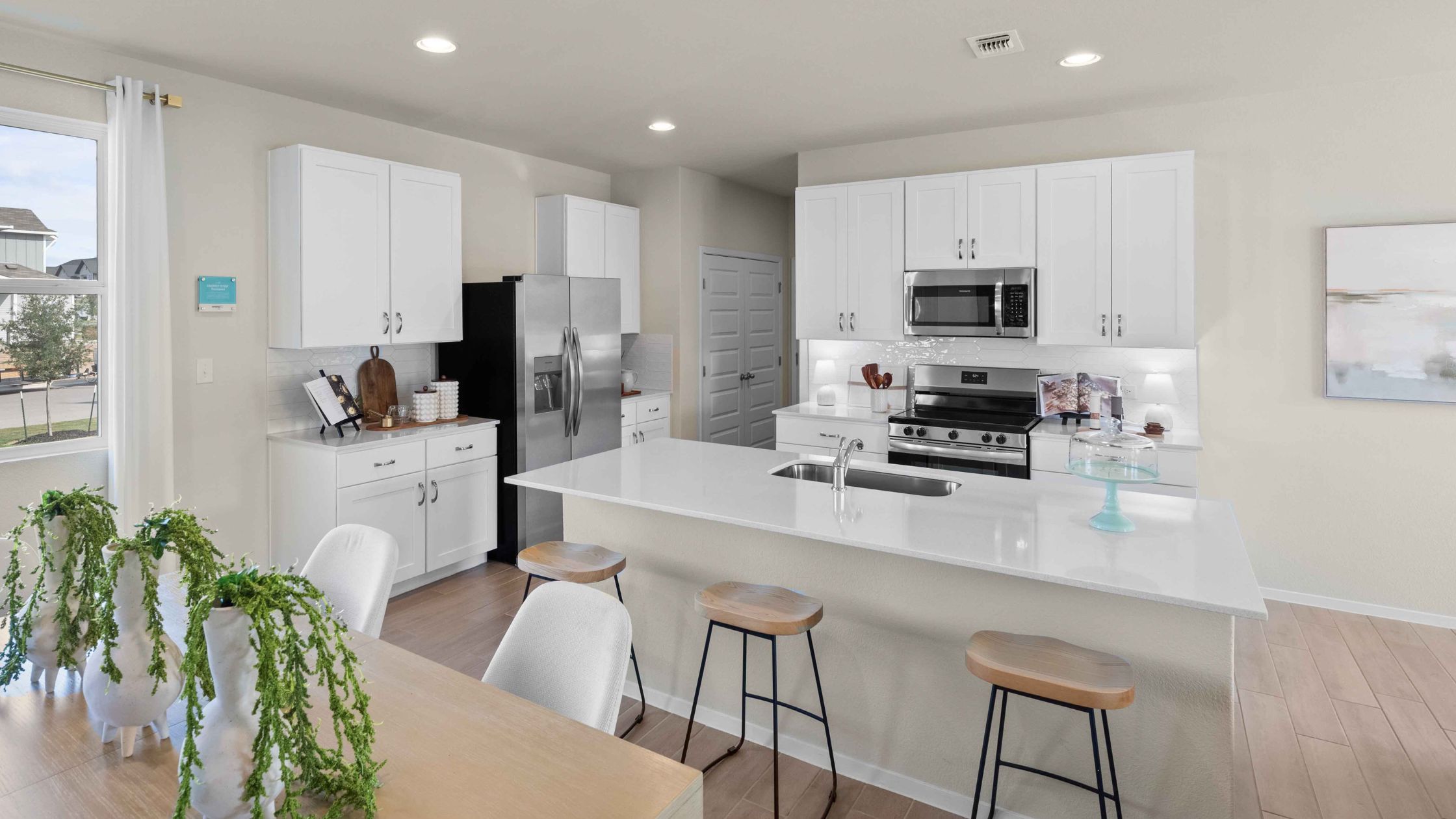 An interior image of a tan dining table view of the kitchen with vinyl flooring, white cabinets and countertop.
