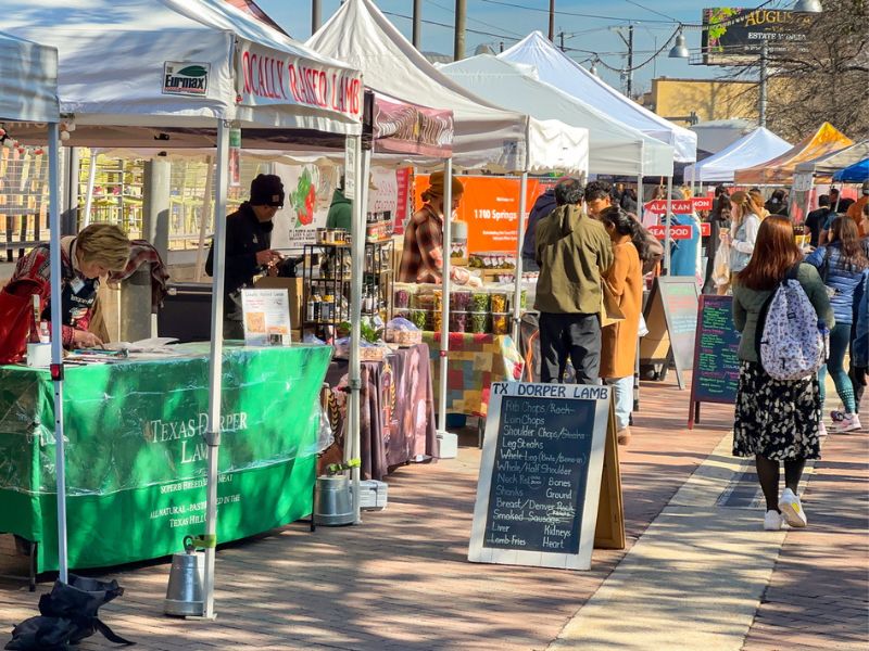 A picture of busy farmers market with white tents and people walking and visiting the tents.