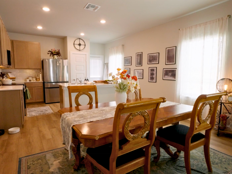 An image of kitchen with brown wood-like vinyl flooring, brown cabinets with white granite counters, and an island with a brown dining room set with four chairs, and various decorations on the wall.