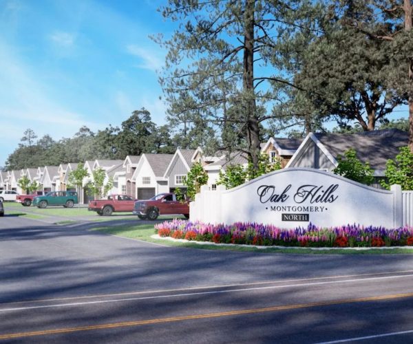 Image of a neighborhood with single-sotry houses, paved roads, cars and trucks, green grass, trees, and a monument stone sign with the words "Oak Hills, Montgomery, an North in dark brown letters with a blue sky in the background.