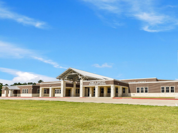 An image of school building with paved parking lot, grass, and blue sky with clouds.