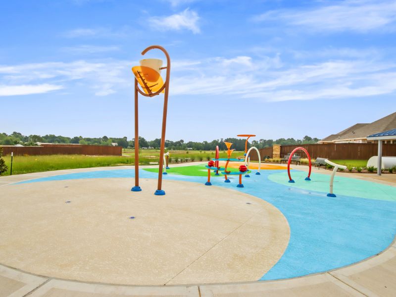 An image of splash pad with a blue and green swirl pattern and yellow and red water attractions, with a blue sky with white clouds in the background.